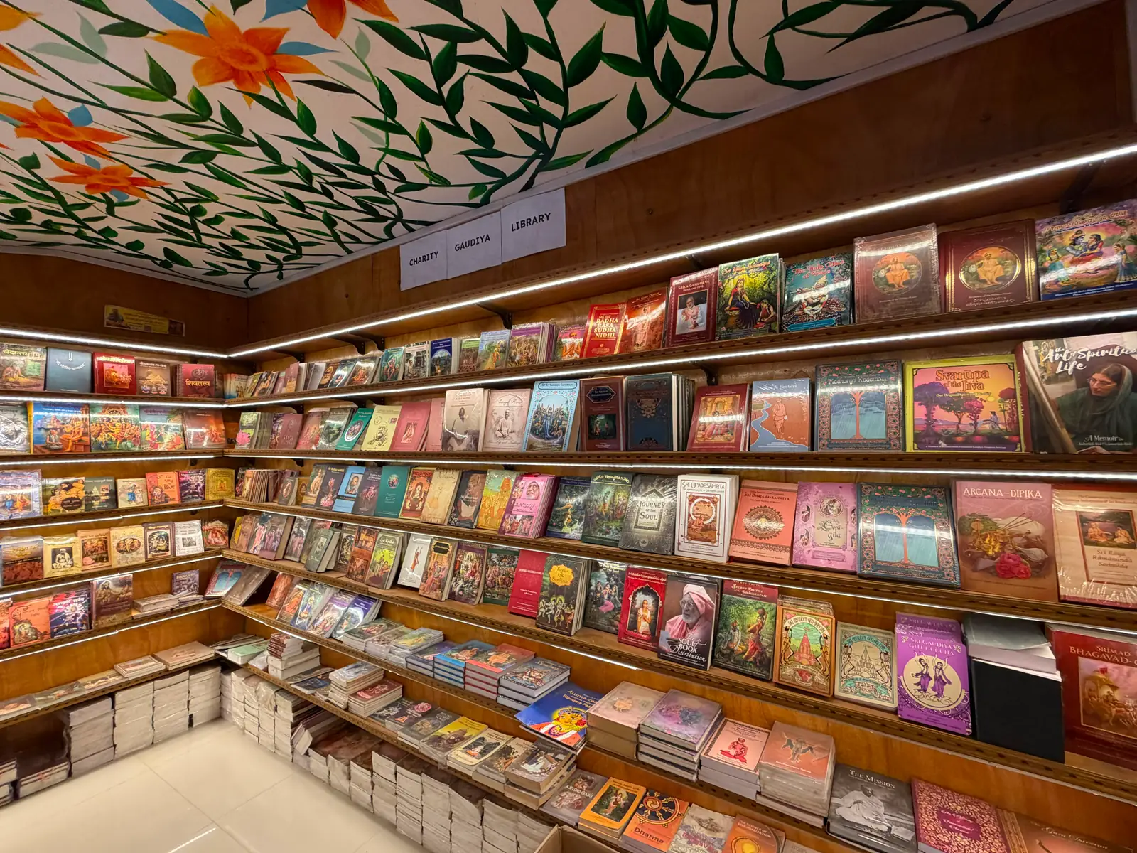 Inside the Bhakta Bandhav bookstore in Vrindavan, shelves stocked with devotional books beneath a hand-painted floral ceiling