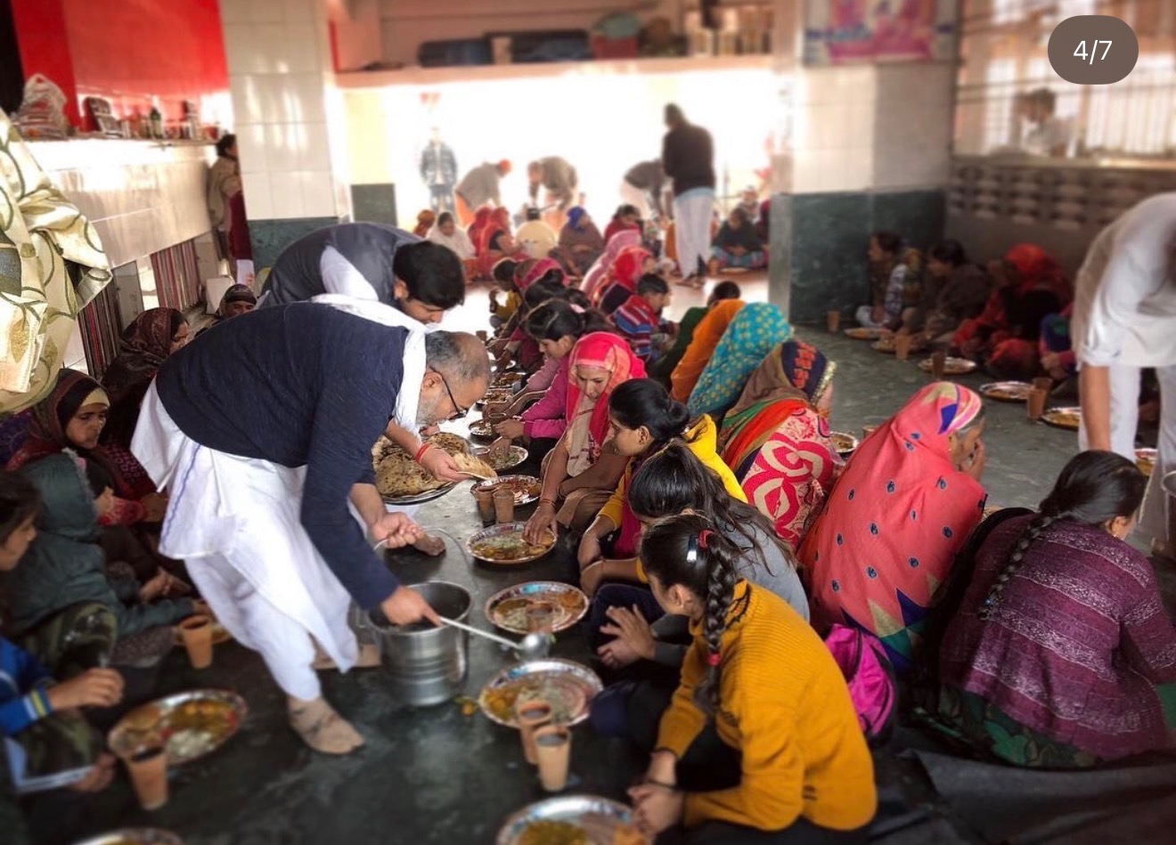 Serving lovingly prepared prasadam to Vrajavasi families seated in rows at Radhe Kunj